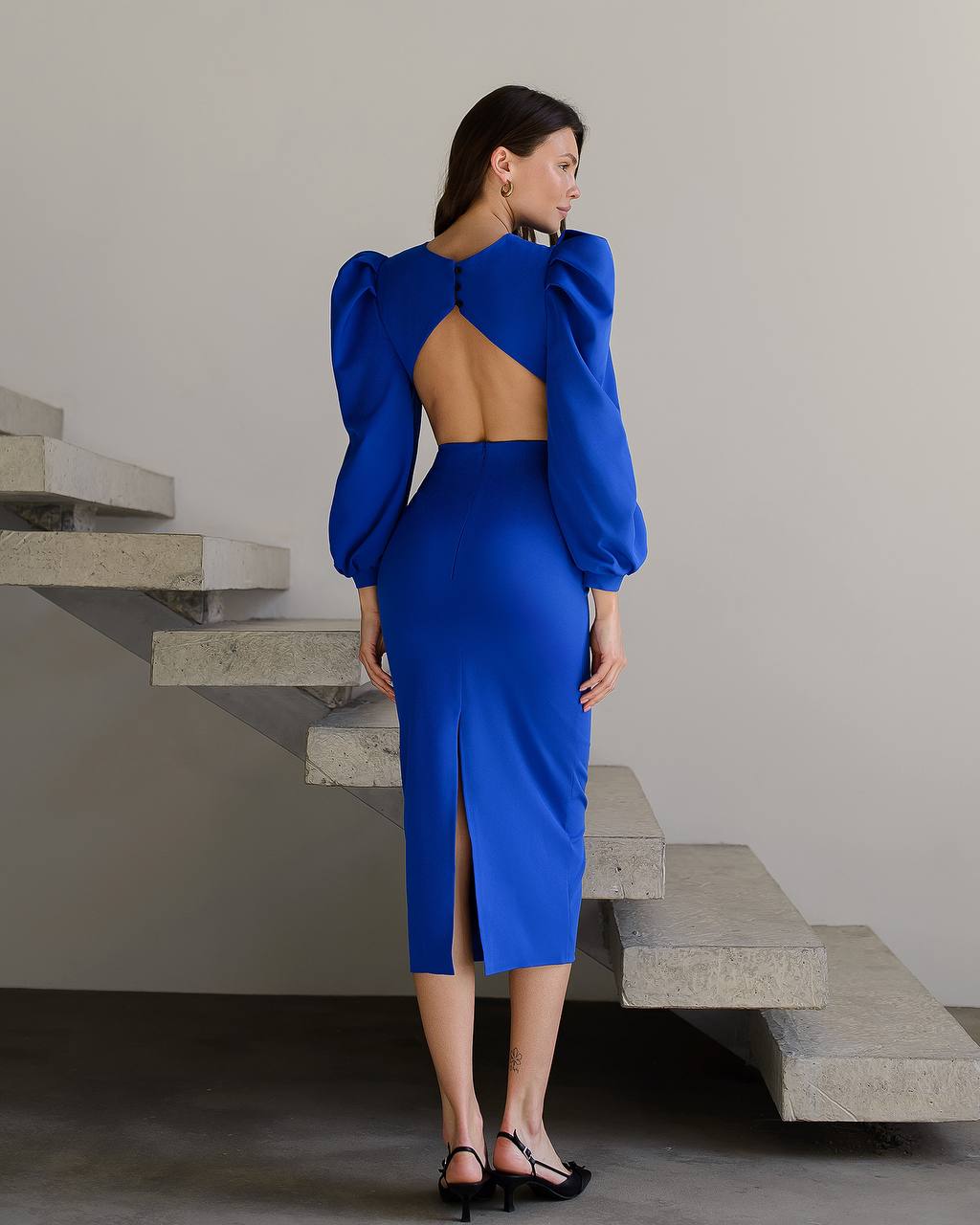 Woman in a blue dress standing on concrete stairs with a neutral background