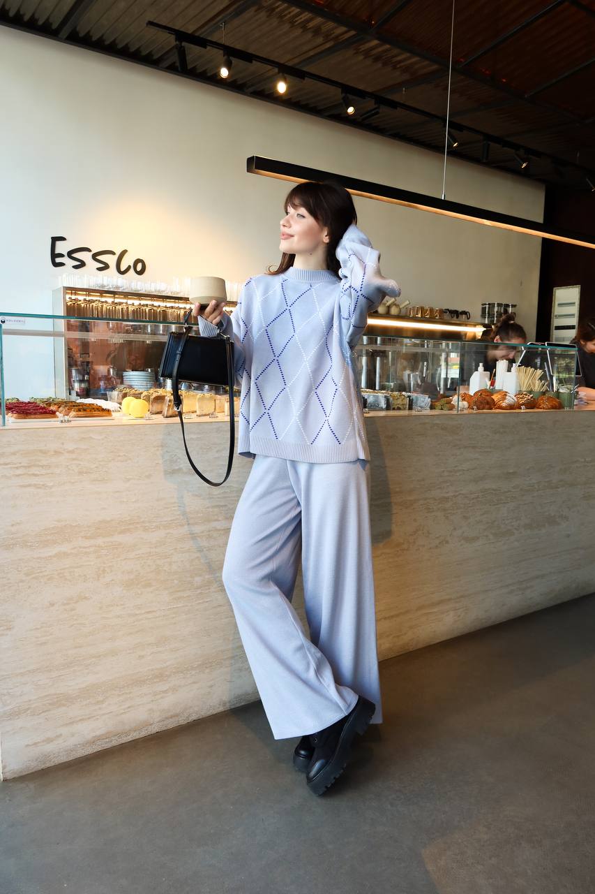 Woman in a light gray outfit standing in a cafe with 'Essco' branding.
