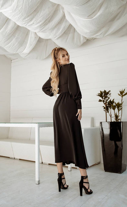 Woman in a black dress standing in a modern interior setting with white walls and a plant.