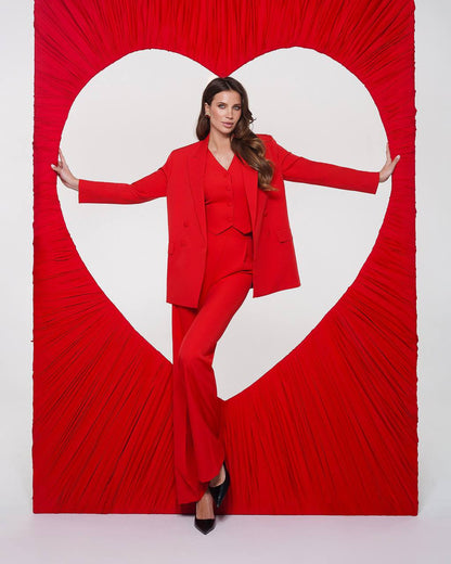 Woman in a red suit standing in front of a heart-shaped cutout on a red background
