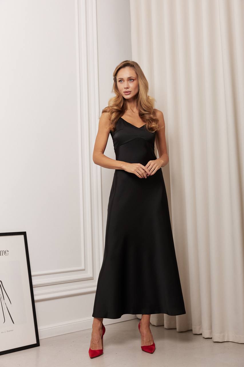 Woman wearing a black dress standing in a room with white walls and curtains.
