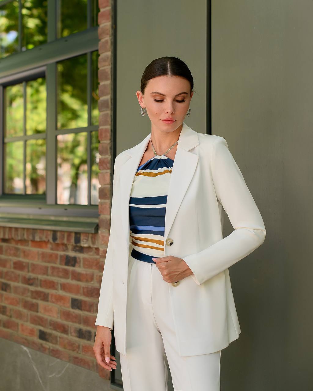 Woman wearing a white suit with a colorful striped shirt in an outdoor setting.