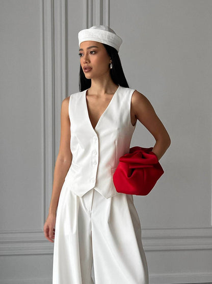 Woman in a white outfit holding a red clutch against a gray wall