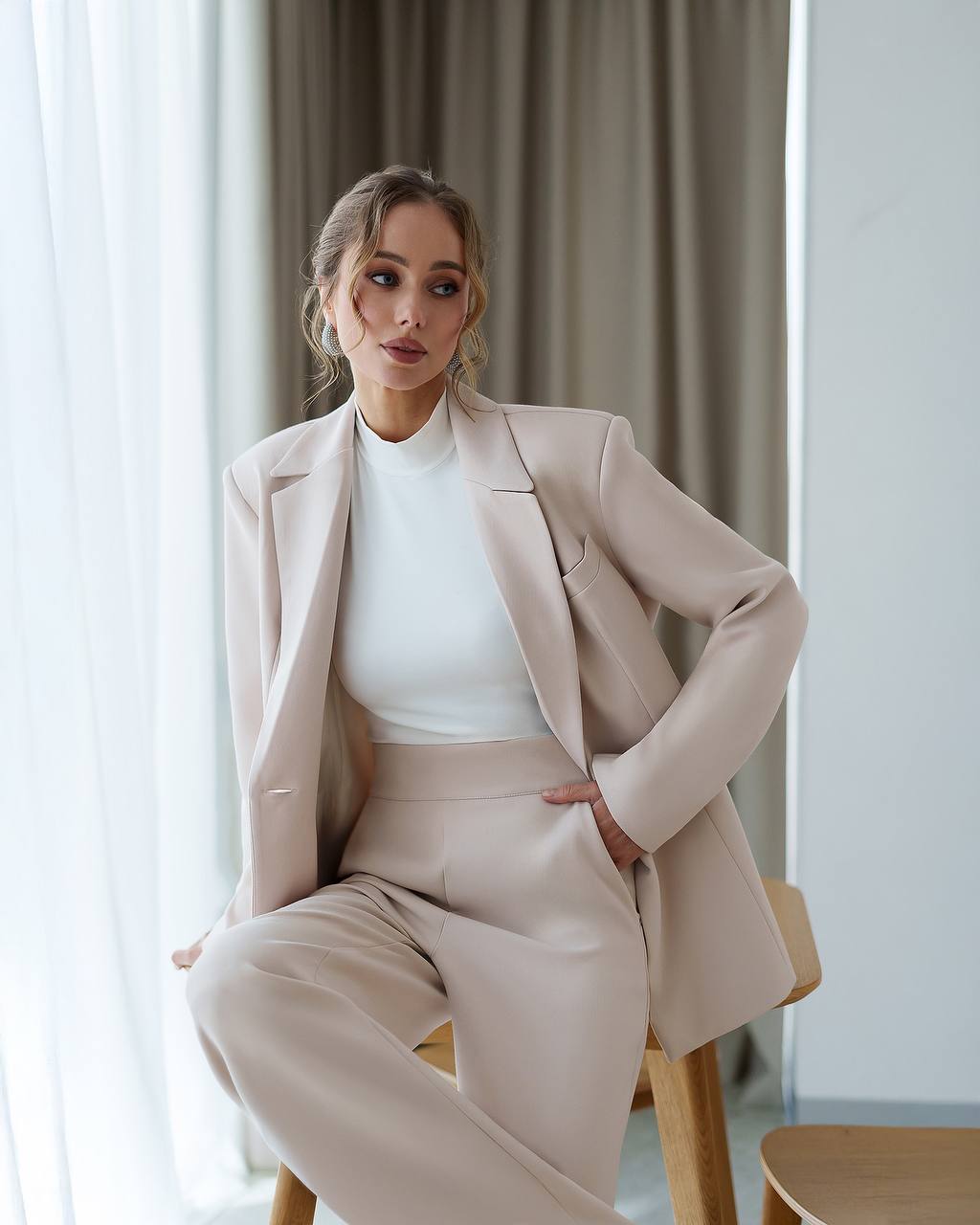 Woman in a beige suit sitting on a chair with a neutral background