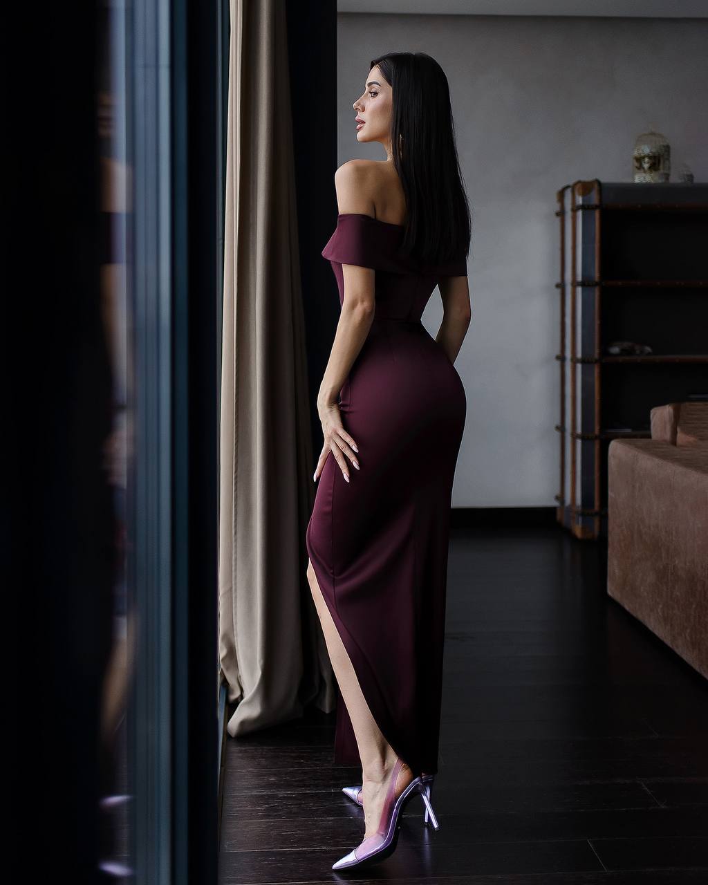 Woman in a burgundy off-shoulder dress standing in a dimly lit room.