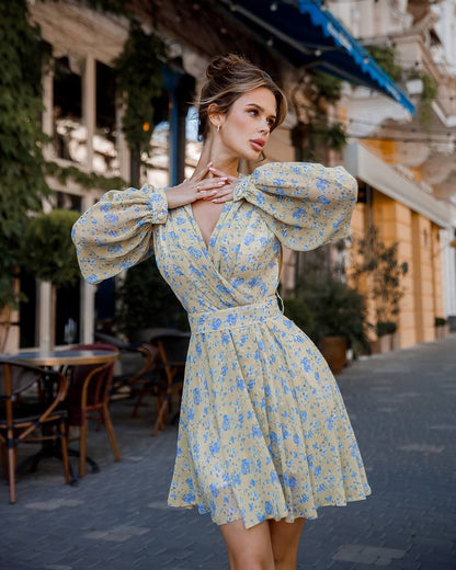 Woman in a floral dress standing on a street with buildings and tables in the background