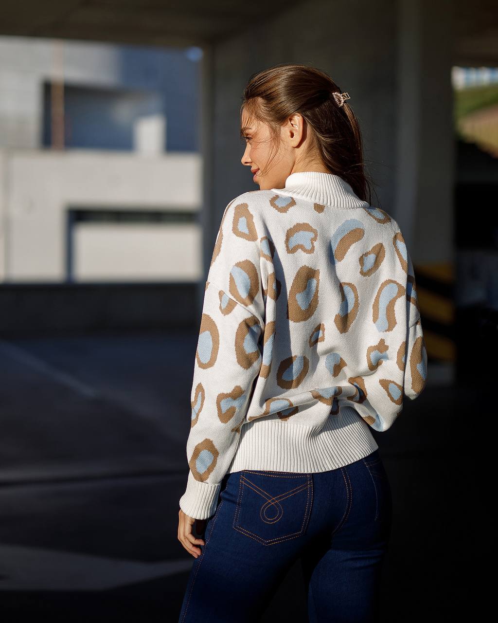 Woman wearing a patterned sweater and blue jeans standing outdoors.