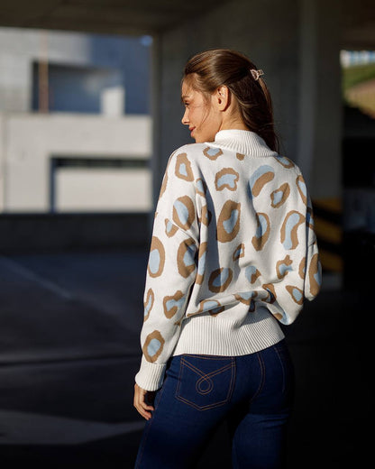 Woman wearing a patterned sweater and blue jeans standing outdoors.