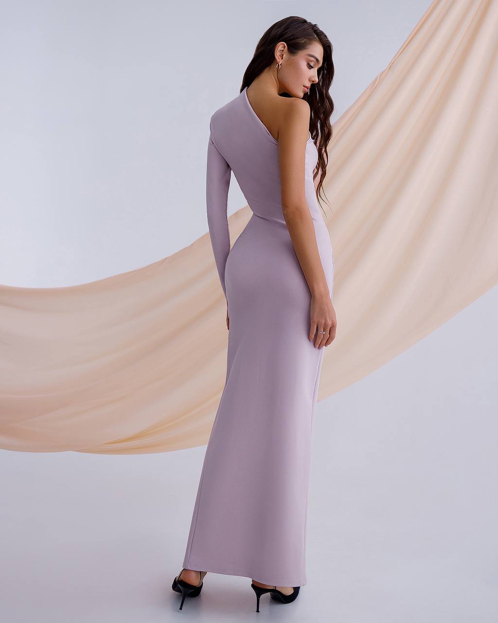 Woman wearing a long, light purple dress with a flowing fabric backdrop.