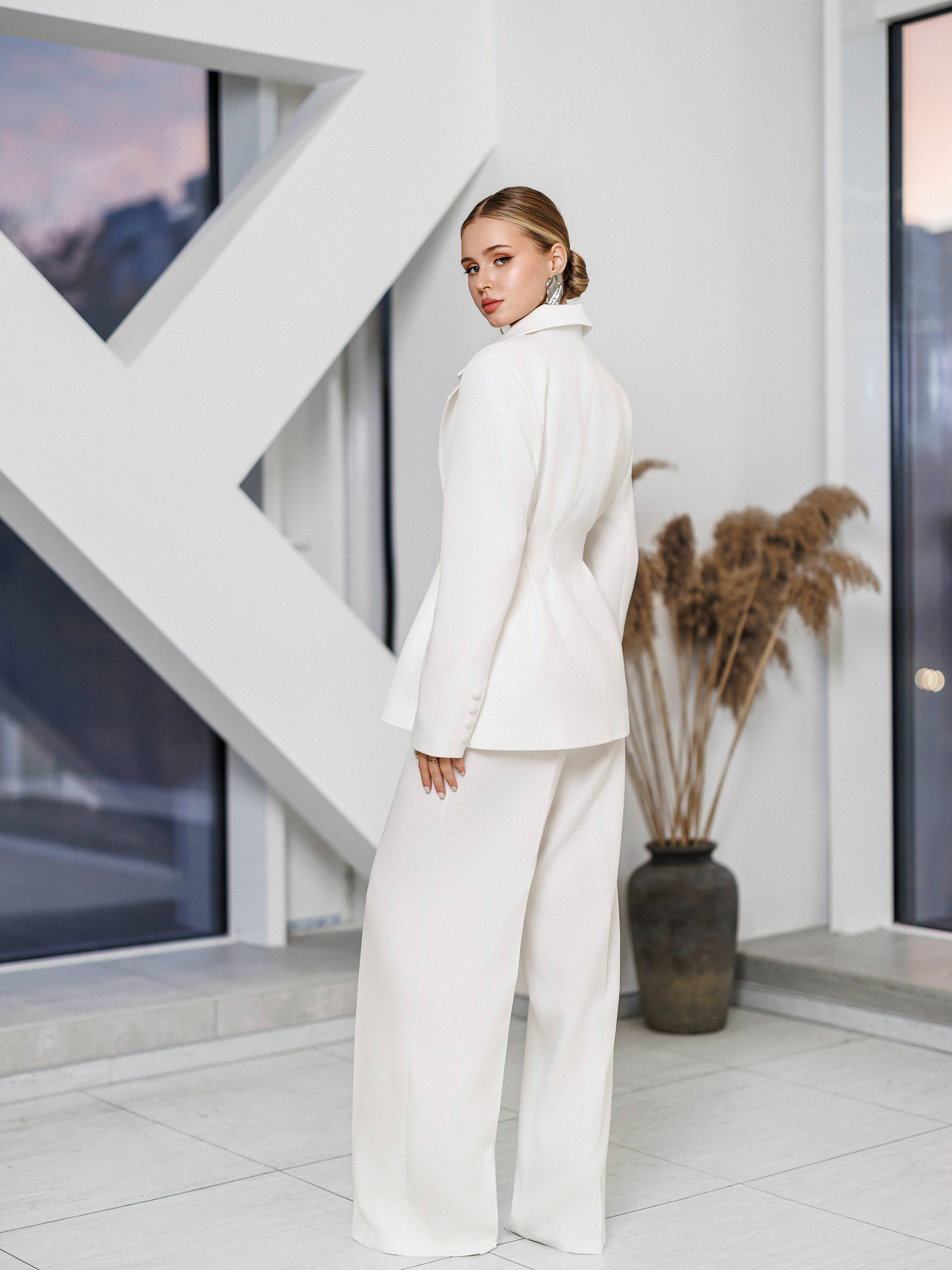 Woman in a white outfit standing in a modern indoor setting with geometric wall design.
