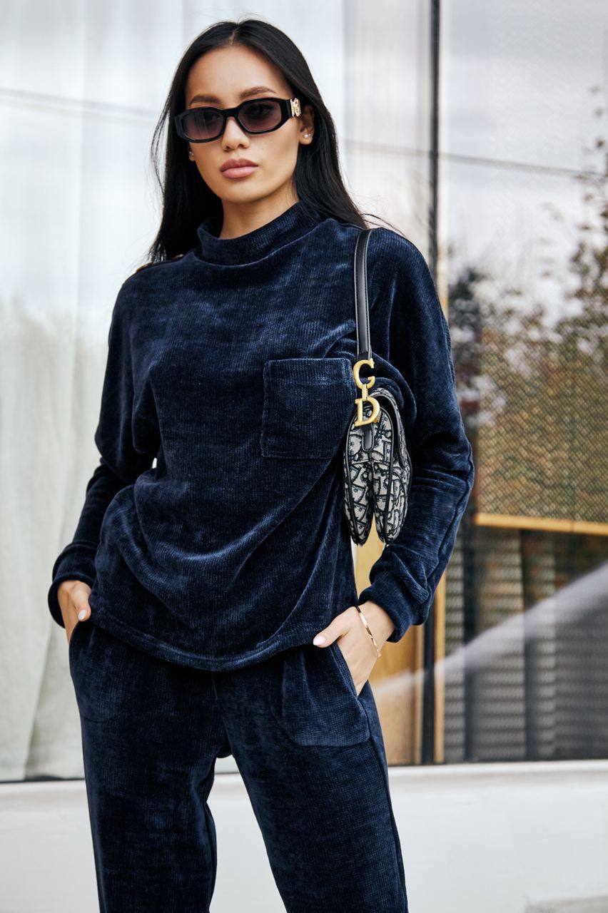 Woman wearing a navy velvet outfit with sunglasses and a handbag, standing outdoors.