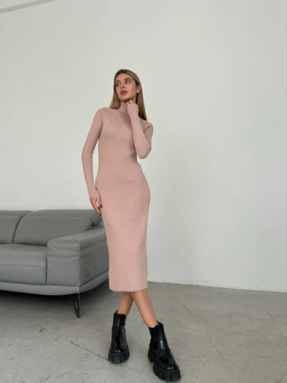 Woman wearing a pink dress and black boots standing in a minimalistic room with a gray sofa.