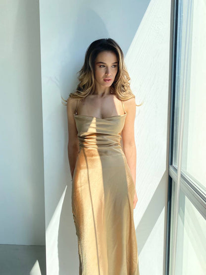 Woman in a gold dress standing against a light-colored wall.