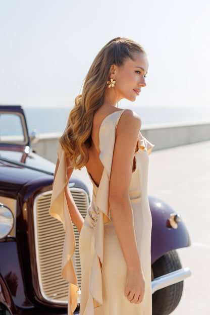 Woman in a beige dress standing next to an old car with a scenic background