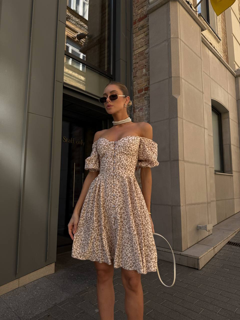Woman in a floral off-shoulder dress standing outside a building.