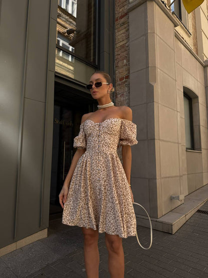 Woman in a floral off-shoulder dress standing outside a building.