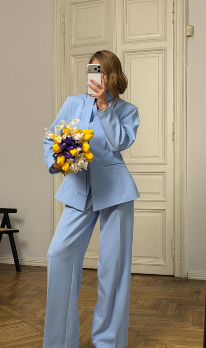 Person wearing a light blue suit holding a bouquet of flowers indoors.
