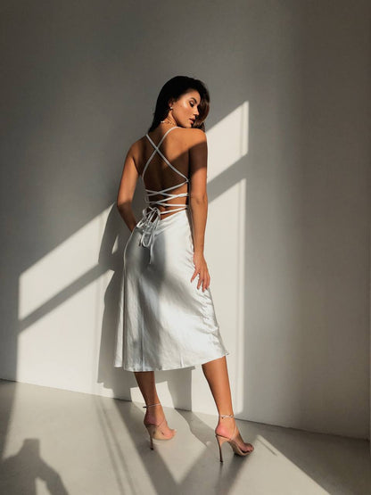 Woman in a white dress standing in a sunlit room with shadows on the wall.