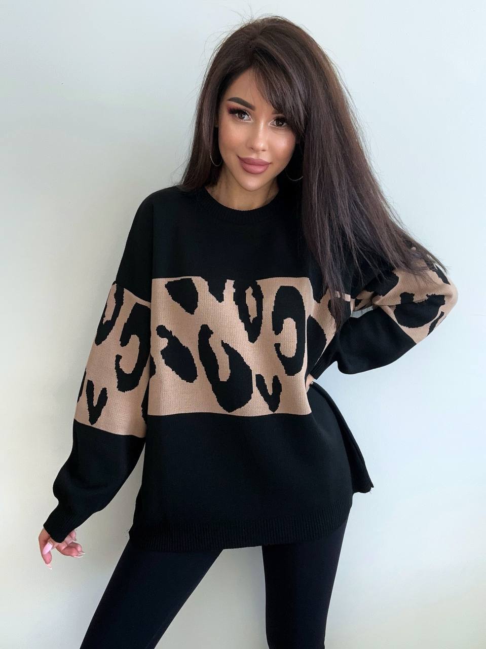 Woman wearing a black sweater with leopard print sleeves against a white background