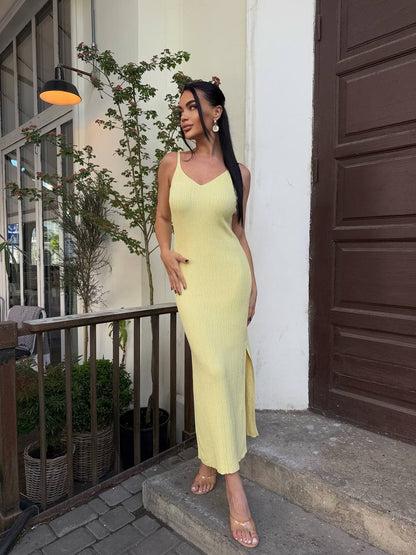 Woman in a yellow dress standing on a balcony with plants and a building in the background