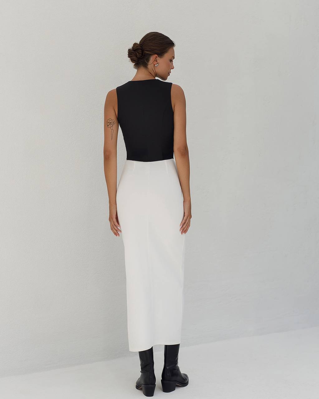 Woman wearing a black top and white skirt on a plain background