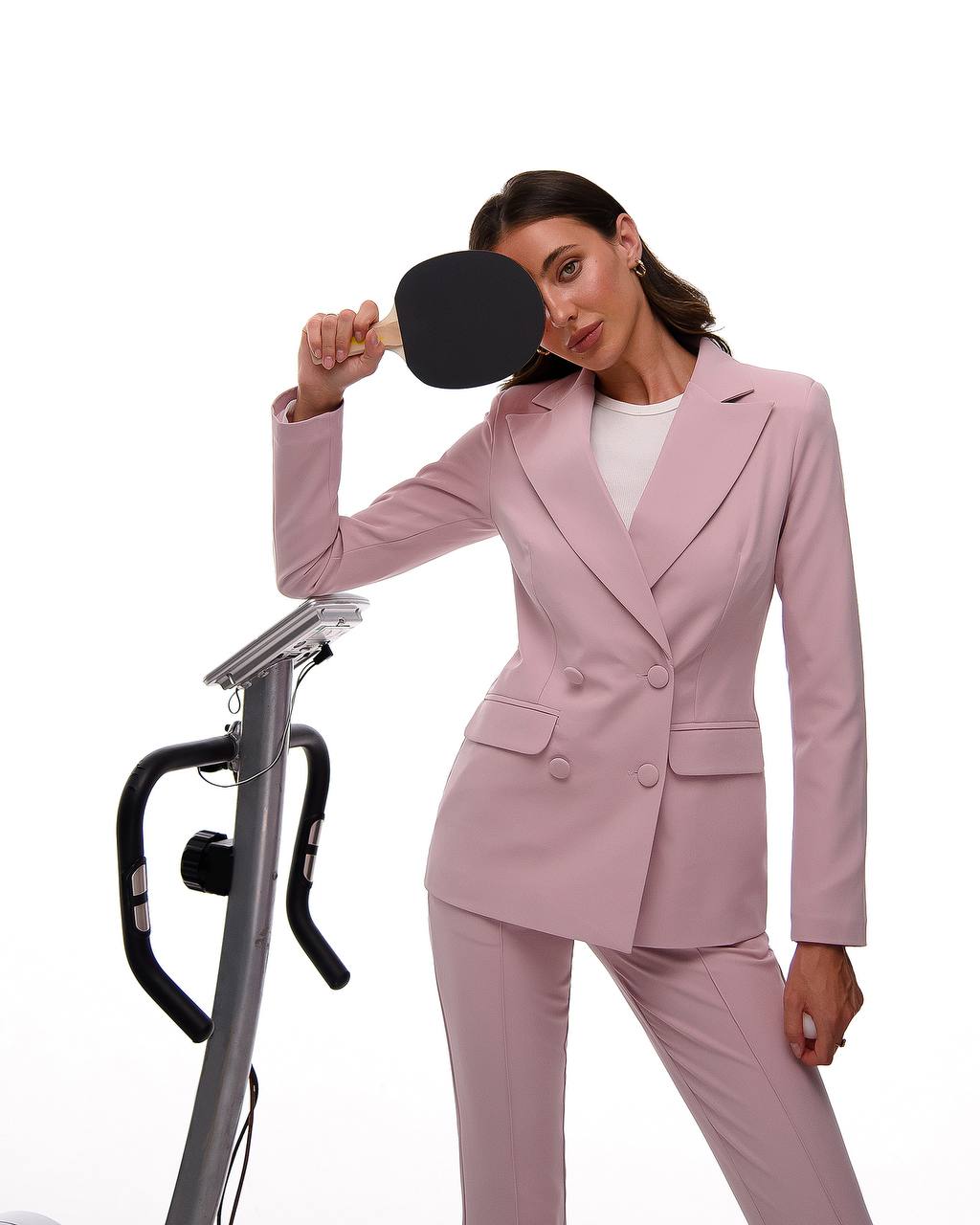 Woman in a pink suit holding a ping pong paddle on a white background