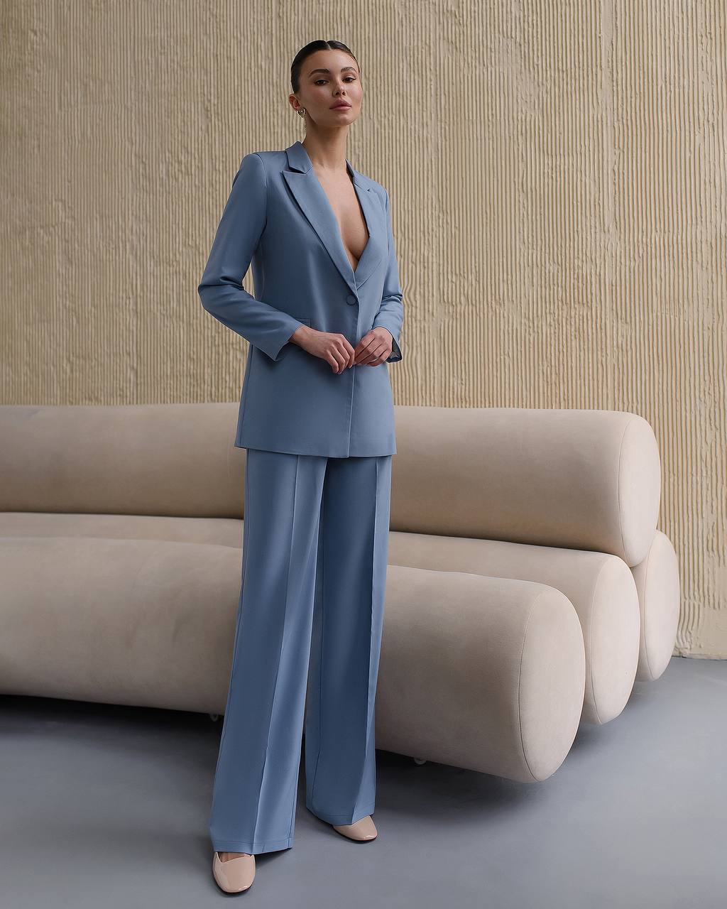 Woman in a blue suit standing in a modern interior setting with beige sofas.