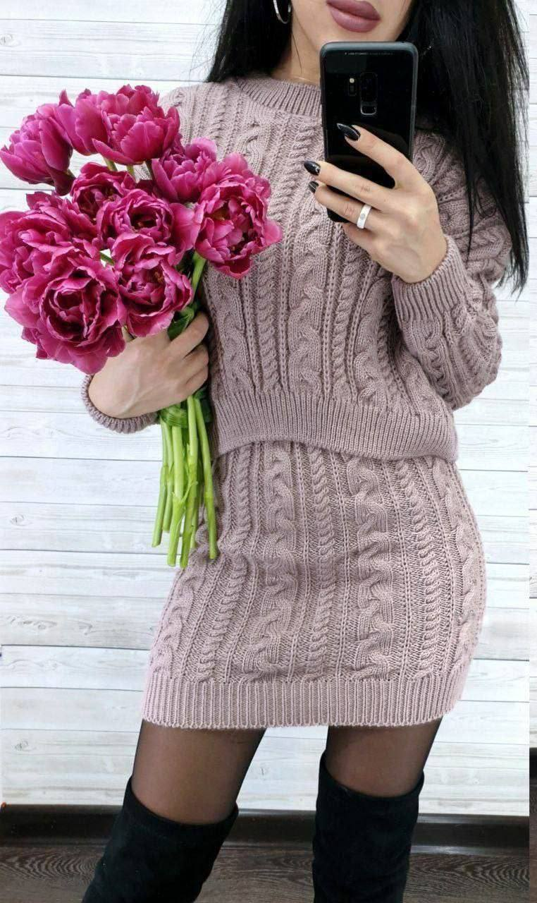 Person wearing a pink knitted dress holding pink flowers and taking a selfie.