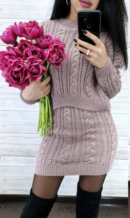 Person wearing a pink knitted dress holding pink flowers and taking a selfie.