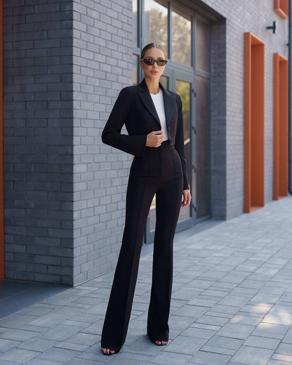 Woman in a black suit standing in front of a gray brick wall.