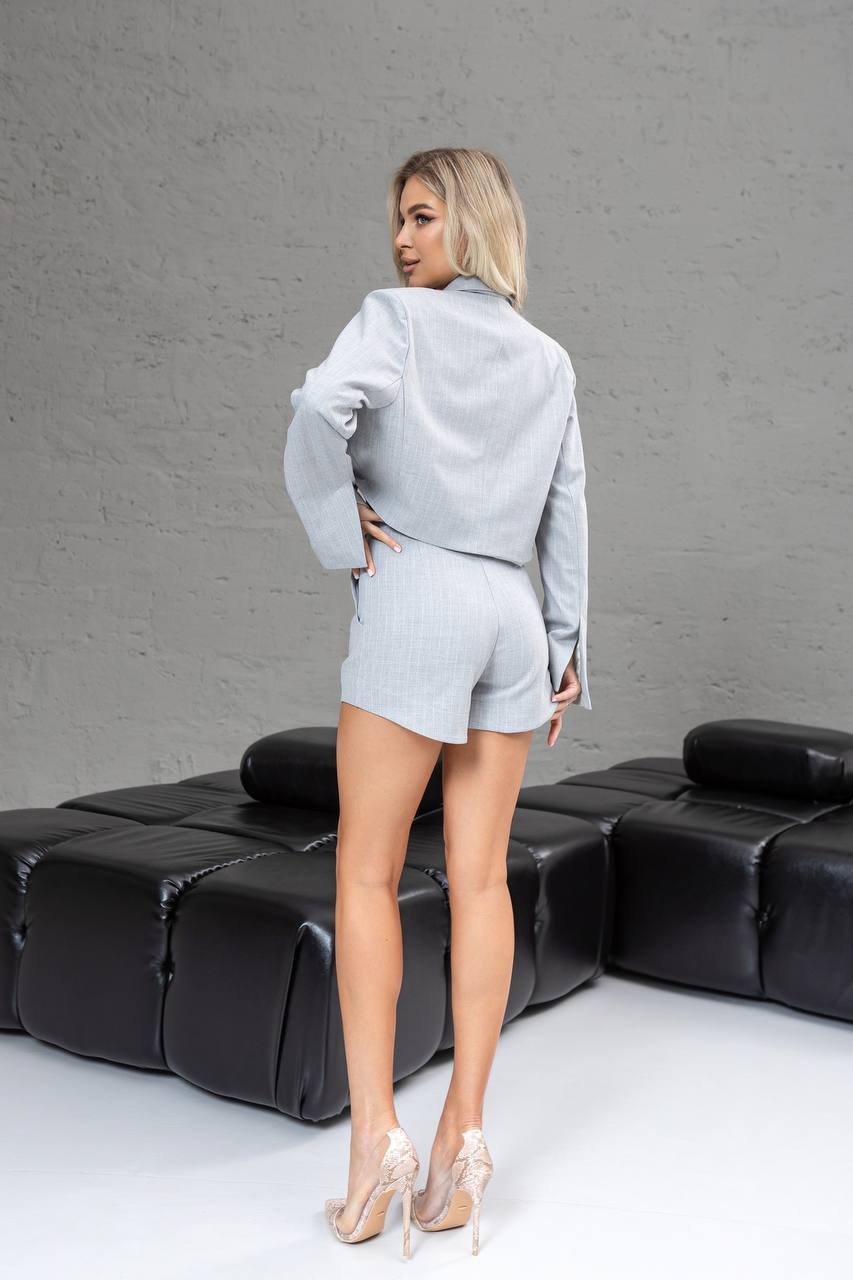 Woman in a gray outfit standing on a black leather couch against a gray wall.