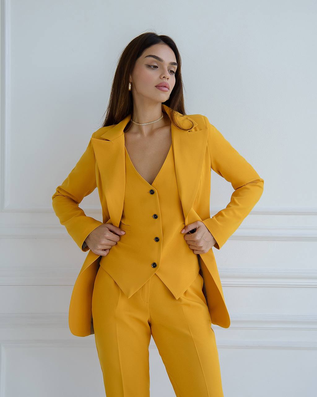 Woman wearing a mustard yellow suit against a white background