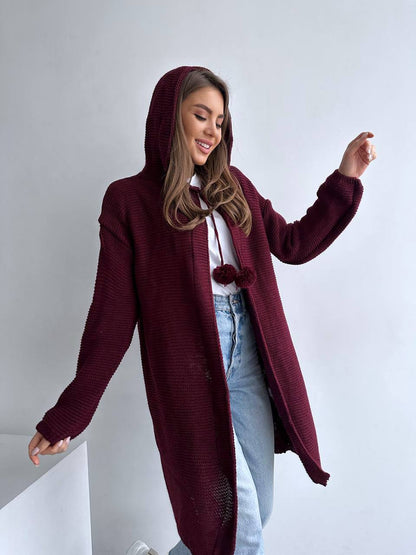 Woman wearing a burgundy hooded coat with pom-pom details on a plain background