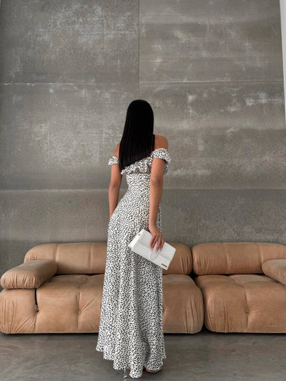 Woman in a patterned dress standing in front of a beige sofa against a gray wall.