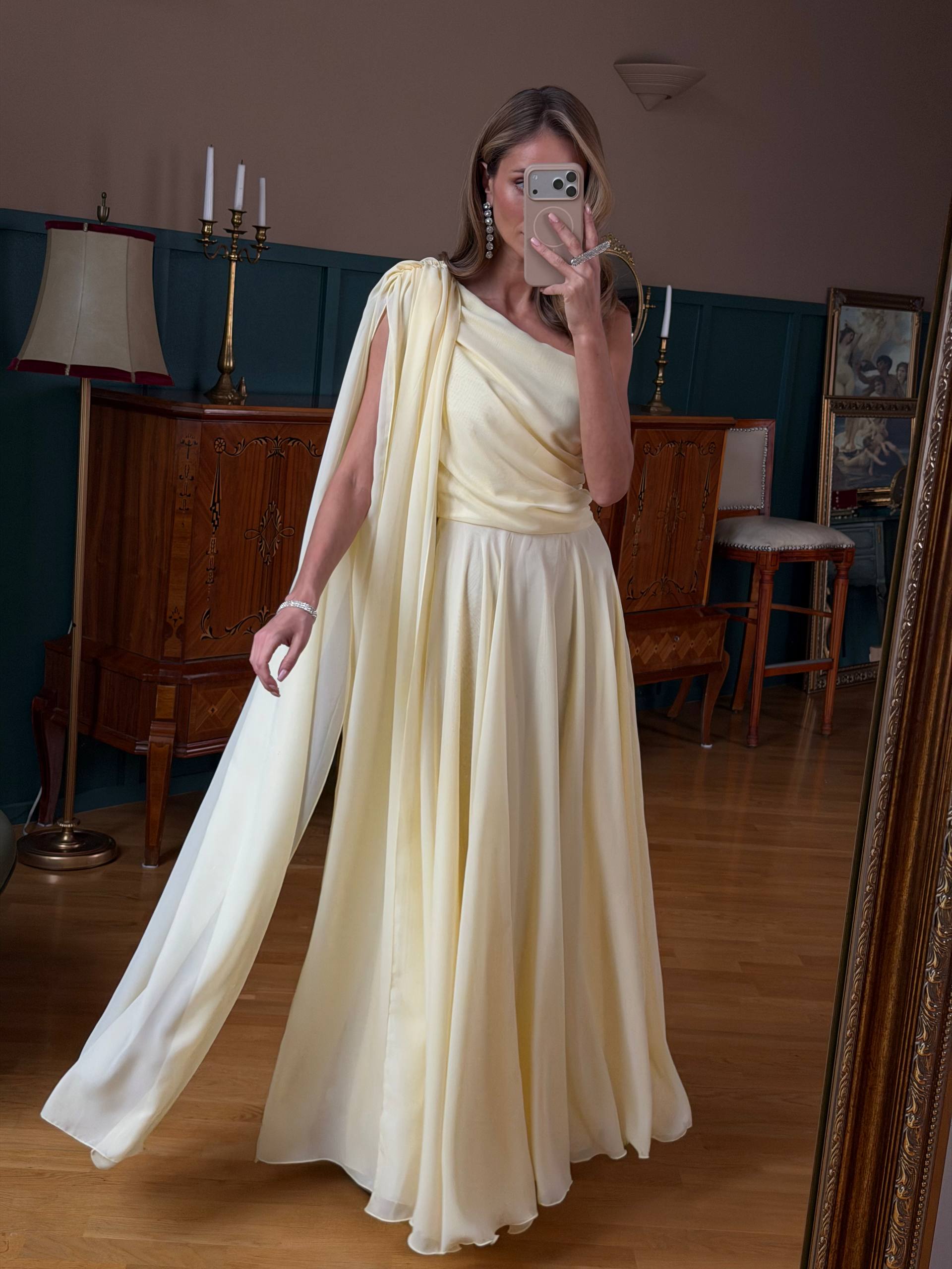 Woman in a long, light-colored dress taking a mirror selfie in an elegant room.