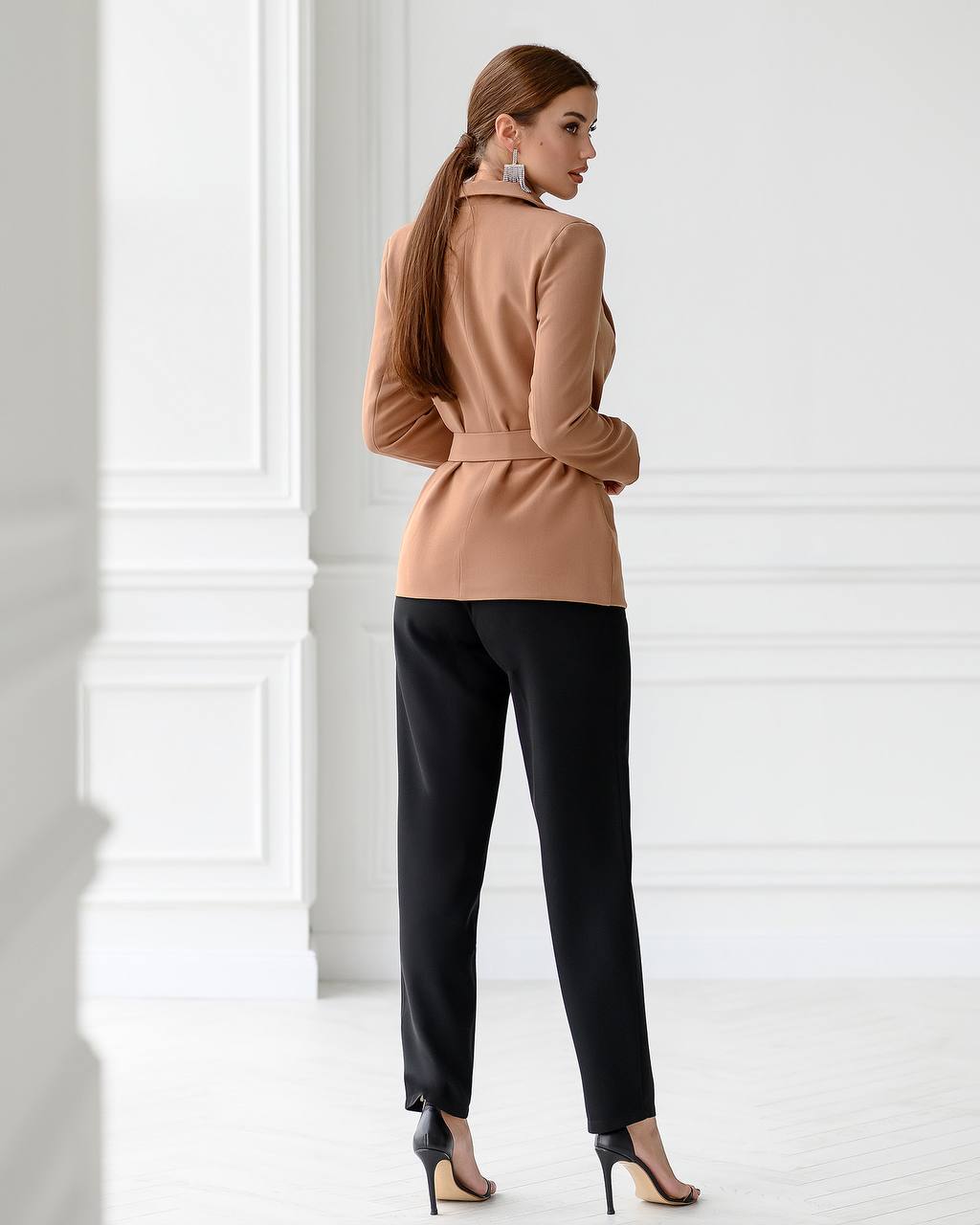 Woman wearing a beige jacket and black pants in a minimalistic setting