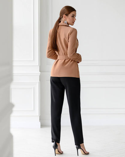 Woman wearing a beige jacket and black pants in a minimalistic setting
