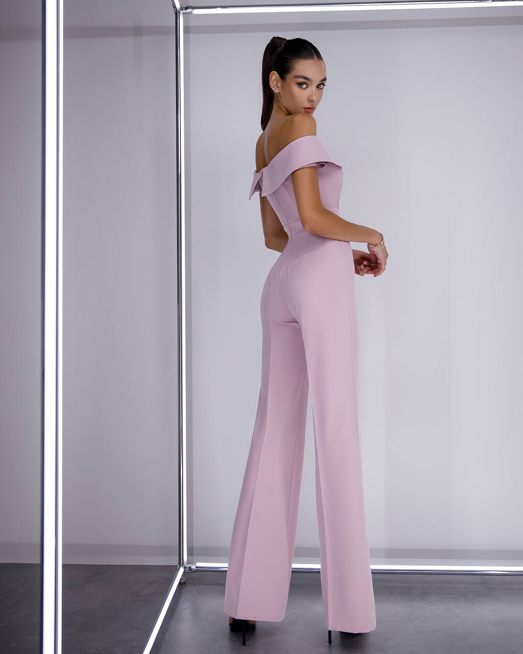 Woman wearing a pink off-shoulder jumpsuit in a minimalistic setting