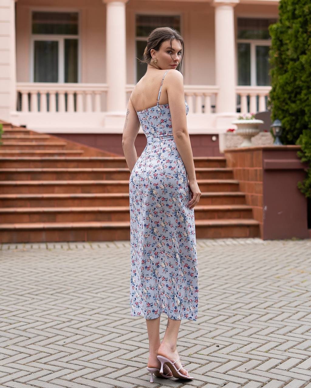 Woman in a floral dress standing on a paved area with steps and greenery in the background