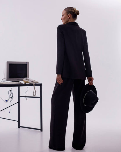 Person in a black suit standing in front of a desk with a computer and phone on a white background