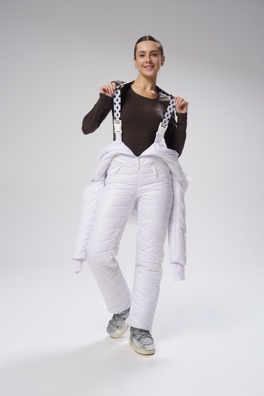 Woman wearing a black long-sleeve top and white overalls on a gray background