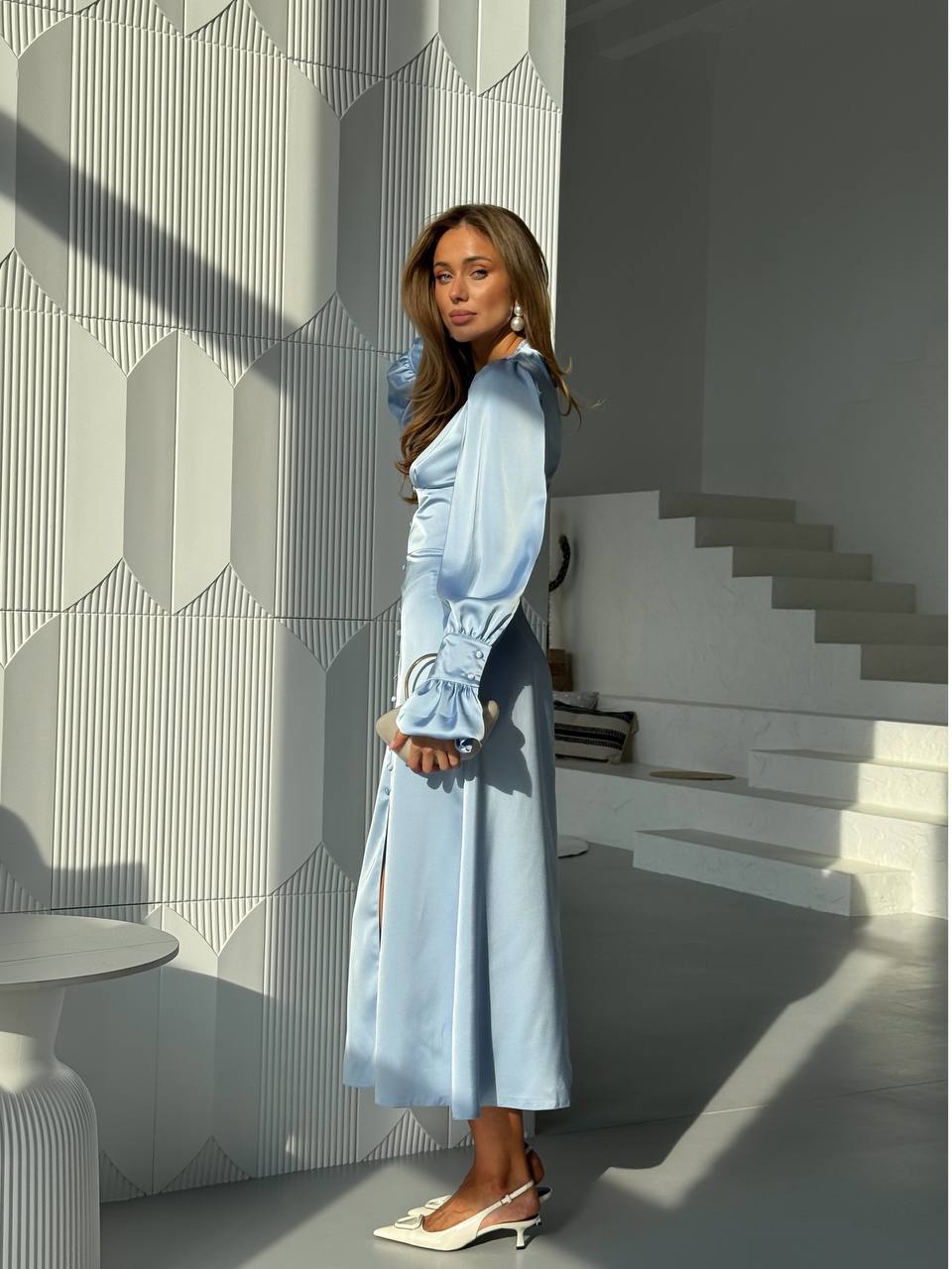 Woman in a light blue dress standing in a modern interior setting with geometric wall patterns.