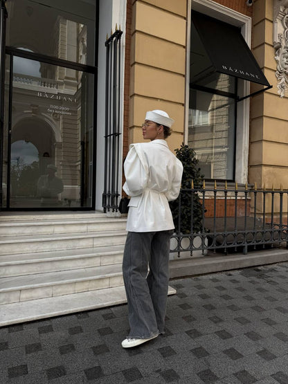 Person in white outfit and hat standing on steps in front of a building entrance.