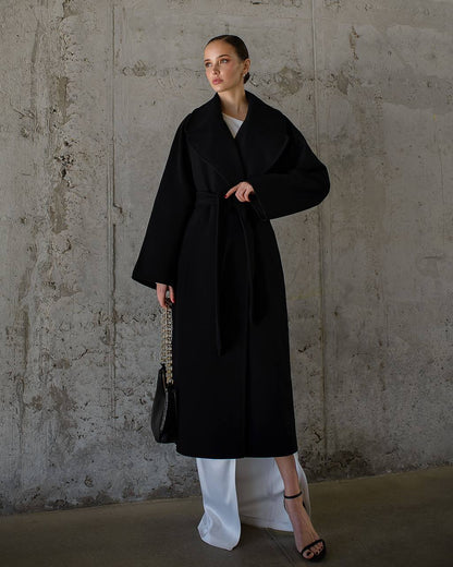 Woman wearing a black coat against a textured wall.