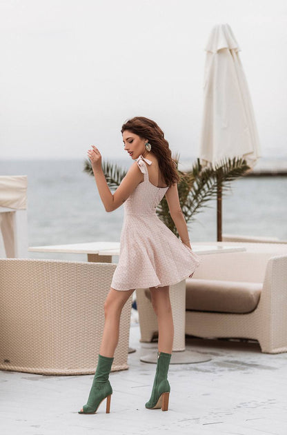 Woman in a light pink dress and green boots standing in an outdoor setting with tables and chairs.