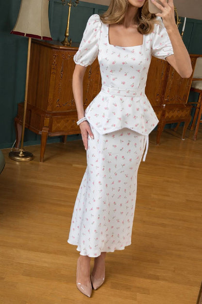 Woman wearing a white floral dress in an indoor setting with wooden furniture.