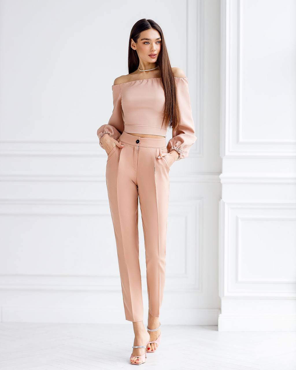 Woman wearing a beige off-shoulder top and pants against a white background