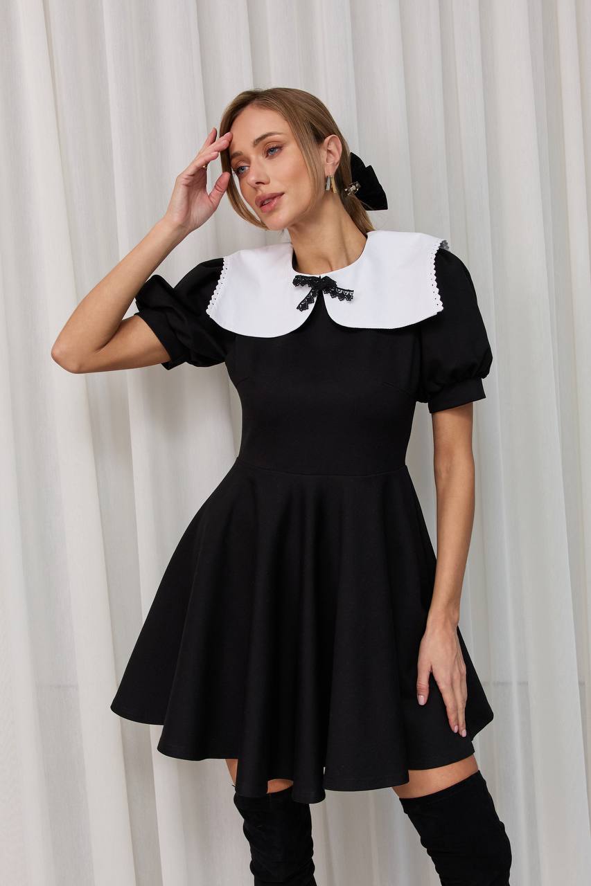 Woman wearing a black dress with a white collar against a white curtain background