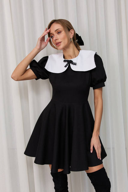 Woman wearing a black dress with a white collar against a white curtain background