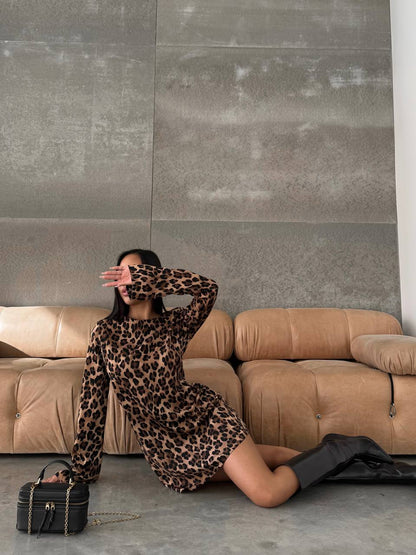 Person wearing a leopard print dress sitting on a beige sofa with a black handbag.